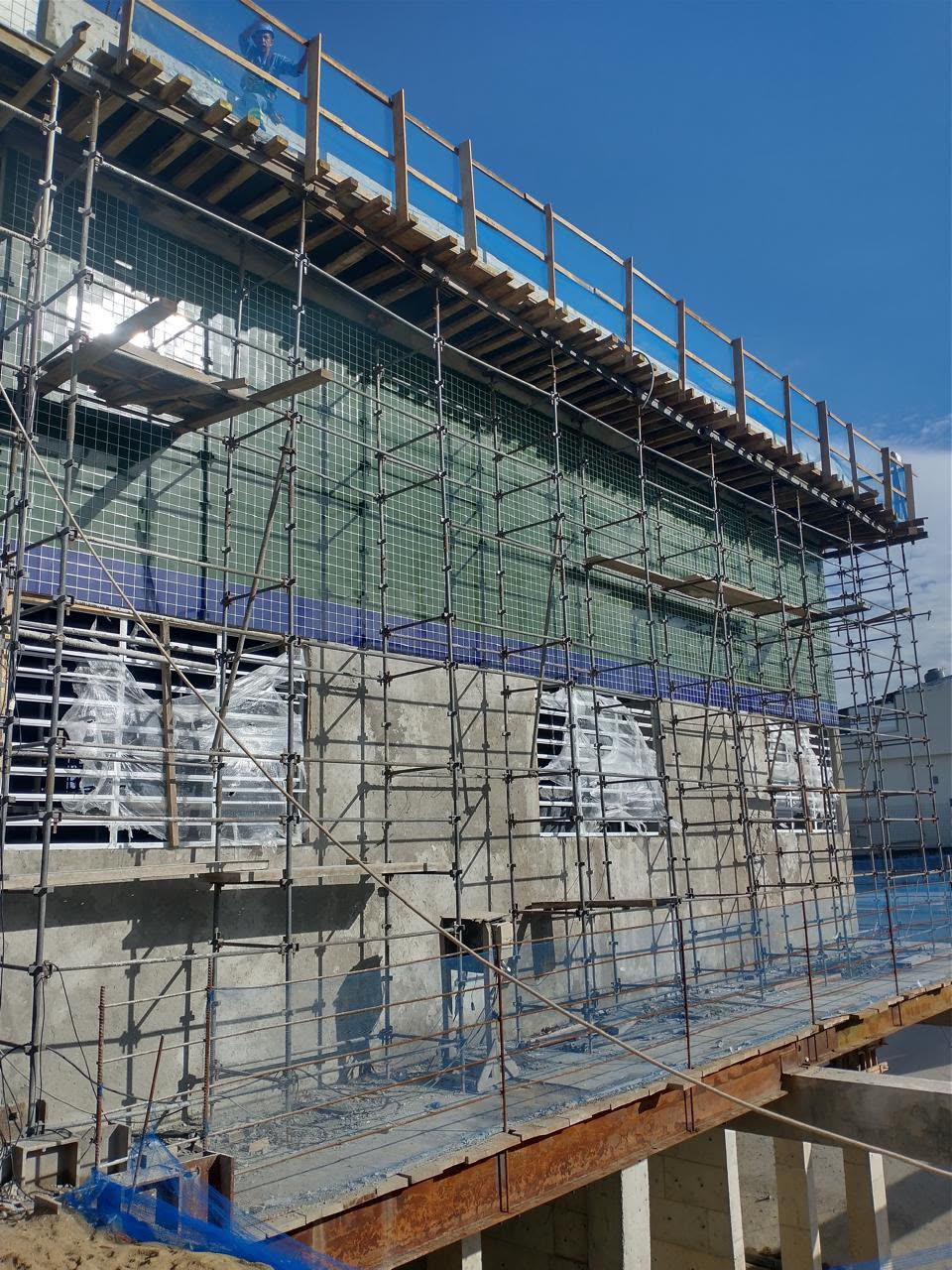 Fachada de edificação em obra com andaimes, escoramentos e revestimento cerâmico em execução
